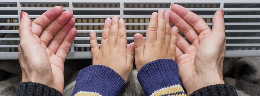 Family warming their hands indoors during cold weather, illustrating home heating comfort and the importance of choosing the right heat pump or central air system for Michigan homes.