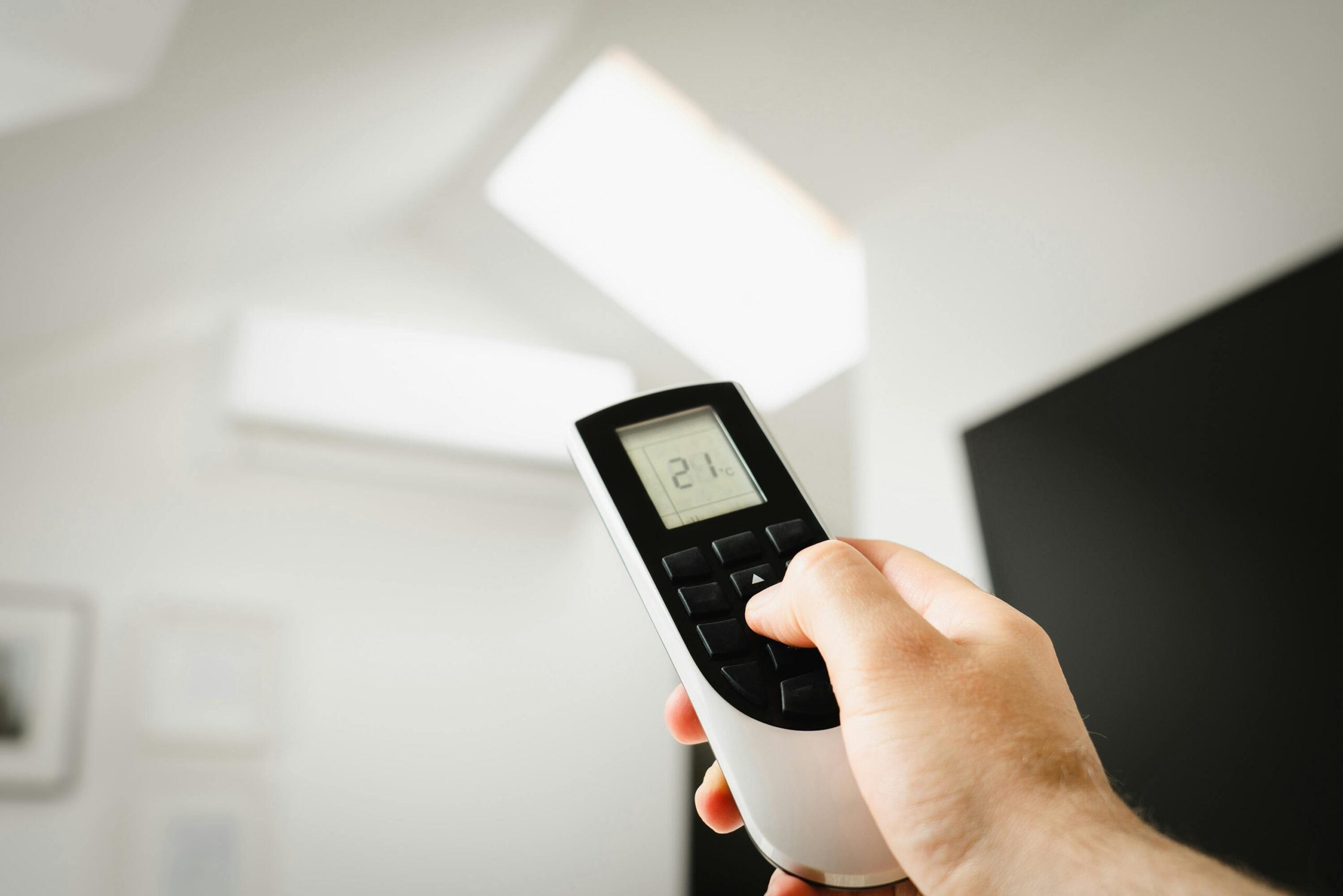 Homeowner adjusting an air conditioner remote control, illustrating seasonal AC maintenance and cooling system preparation for summer in a Detroit-area home.