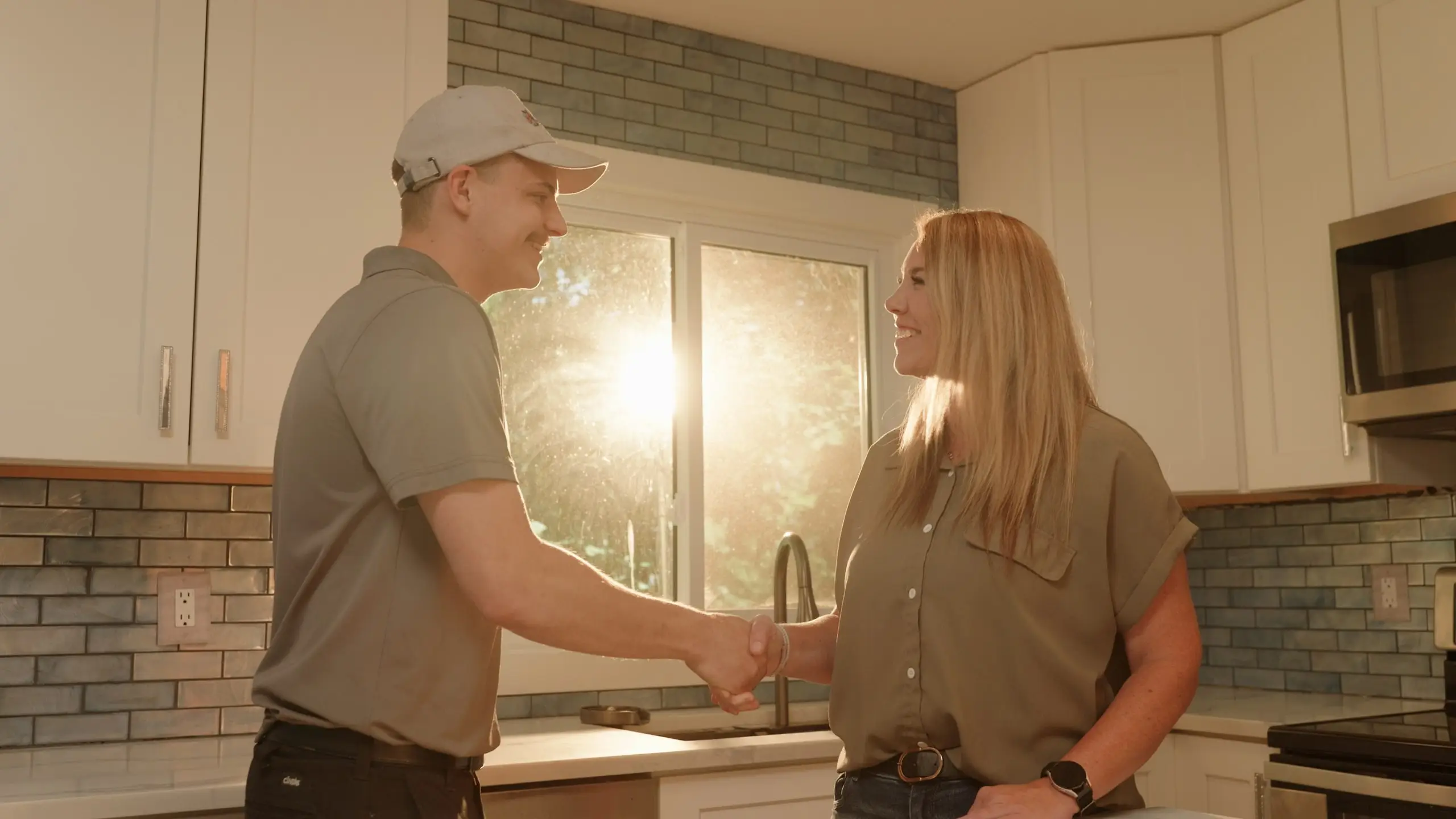 A technician in a uniform and cap smiles at a woman while holding a CREGGER brochure. They stand in a sunlit room, conveying a friendly tone.