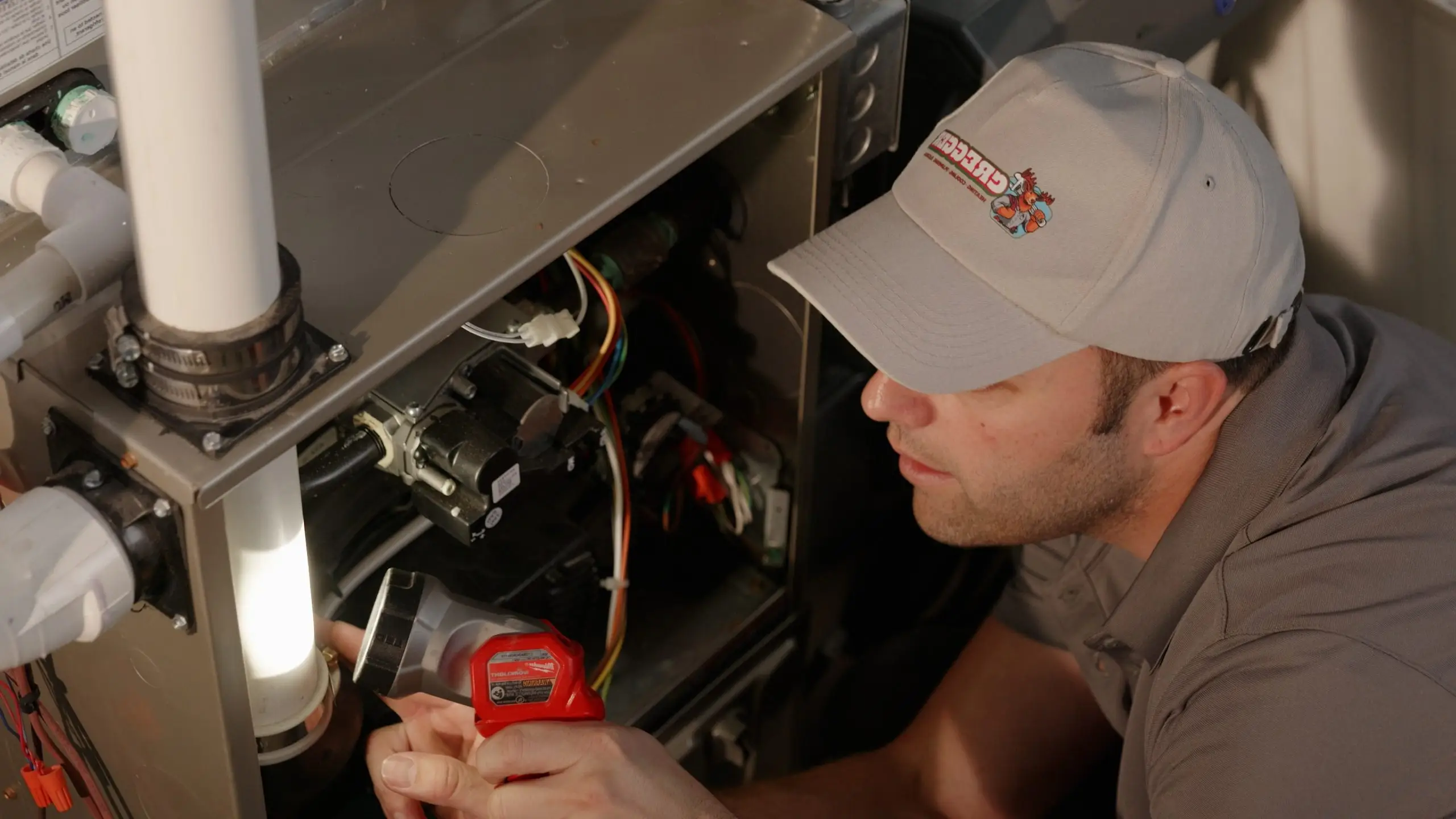 A Cregger technician in a gray cap examines the interior of a furnace, holding a flashlight. The scene is focused and professional, conveying a sense of diligence.