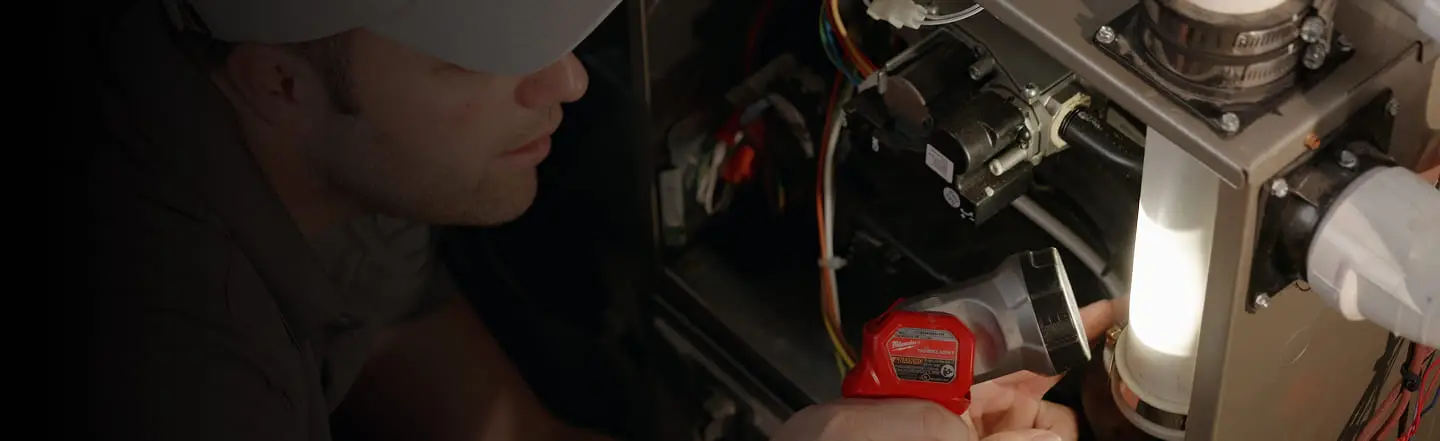 A Cregger technician in a gray cap examines the interior of a furnace, holding a flashlight. The scene is focused and professional, conveying a sense of diligence.